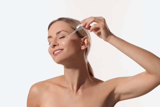 Beautiful woman applying cosmetic serum onto her face on white background - Zdjęcie, obraz