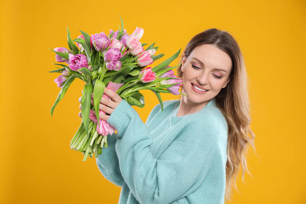 Happy young woman with bouquet of beautiful tulips on yellow background - Фото, зображення