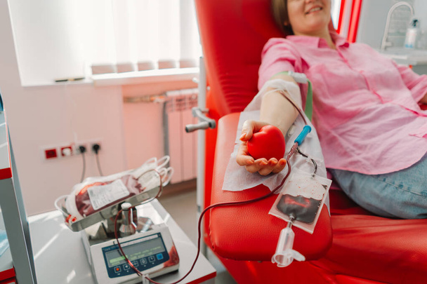 Nuori nainen tekee verenluovutusta sairaalassa. Nainen luovuttaa verta pitäen punaista sydäntä. Verenluovutus. - Valokuva, kuva