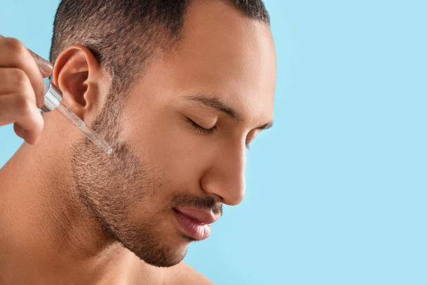 Handsome man applying cosmetic serum onto face on light blue background, closeup. Space for text - Foto, Bild