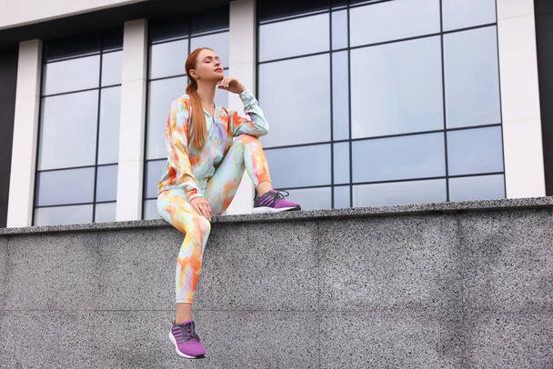 Beautiful woman in gym clothes sitting on parapet on street, space for text - Foto, afbeelding