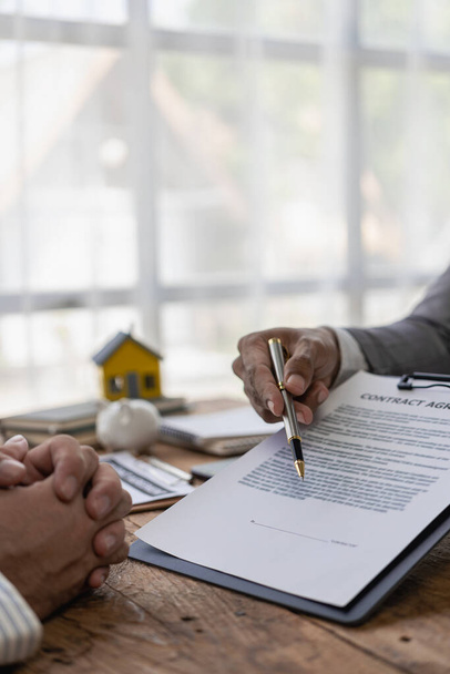 Агент з нерухомості обговорює умови договору купівлі будинку і просить клієнта підписати документ для юридичного укладення договору. вертикальне зображення - Фото, зображення