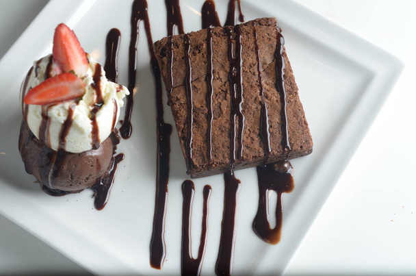 Вкусный шоколадный кекс, пропитанный сиропом и подаваемый с двумя ложками ванильного и шоколадного мороженого.   - Фото, изображение