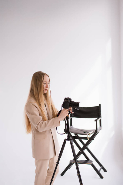 Woman, videographer, photographer, blogger working, shooting video on camera LumixGH5 with tripod. Blonde in business suit on isolated white background in photo studio.Vertical - Foto, Imagen