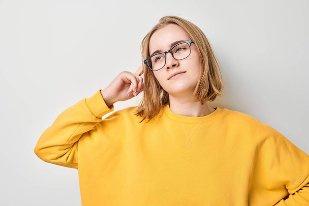 Clever blond student girl with glasses touches head thinks, chooses isolated on white studio background with copy space. Confidence smart genius - Fotó, kép