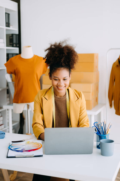 Calm curly brunette dark skinned woman on desk in modern office of fashion designer and working on laptop - Φωτογραφία, εικόνα