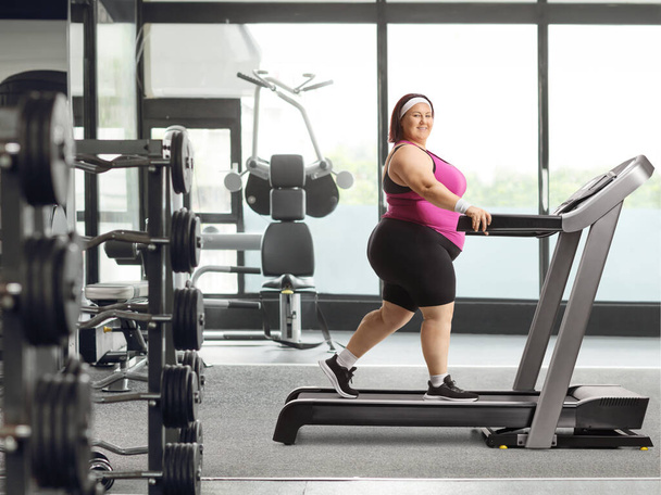 Smiling young overweight woman walking on a treadmill at the gym - 写真・画像
