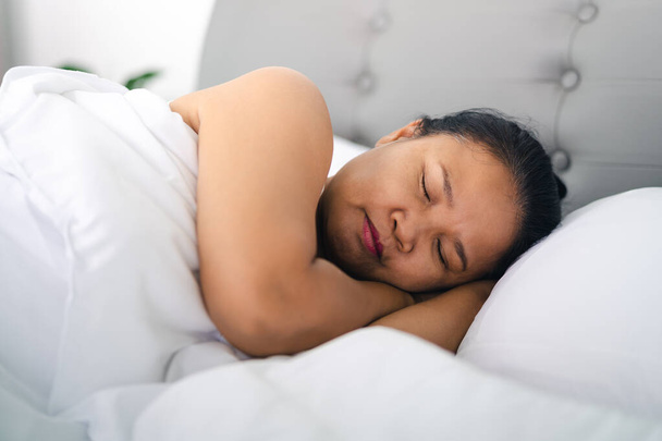 Reife Frau schläft auf dem weißen Bett zu Hause. - Foto, Bild