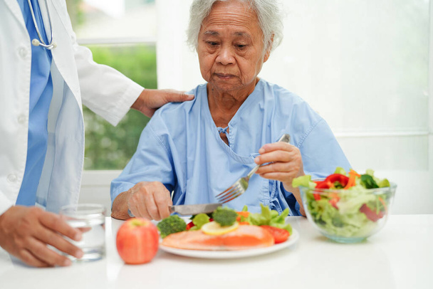 Aziatische oudere vrouw patiënt eten zalm staak en groente salade voor gezond voedsel in het ziekenhuis. - Foto, afbeelding