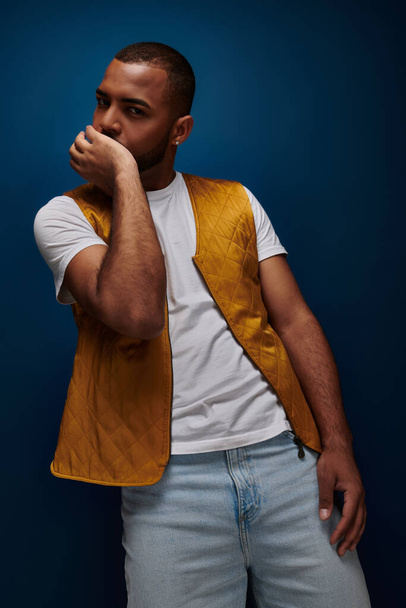 jong Afrikaans amerikaans man model in geel vest poseren met zijn pols op kin, mode concept - Foto, afbeelding