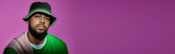 handsome bearded man in green panama on purple backdrop looking at camera, fashion concept, banner - Photo, Image