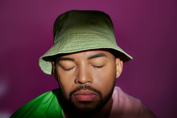 primer plano joven en panama verde con sudadera púrpura atada a los hombros, ojos cerrados, moda - Foto, Imagen