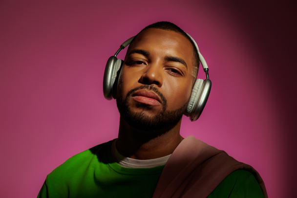 przystojny Afroamerykanin człowiek w bluzie ze słuchawkami na różowym tle, koncepcja mody - Zdjęcie, obraz