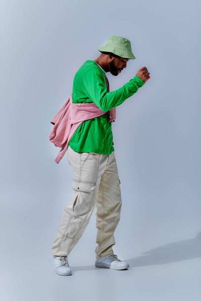 junger bärtiger Mann in stylischem Outfit, der vor hellblauem Hintergrund tanzt und gestikuliert, Modekonzept - Foto, Bild