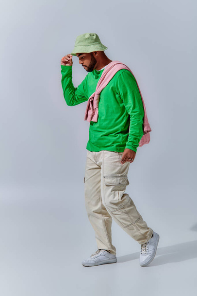 Красивый молодой человек в модной уличной одежде позирует в профиль касаясь своей панамы, концепции моды - Фото, изображение