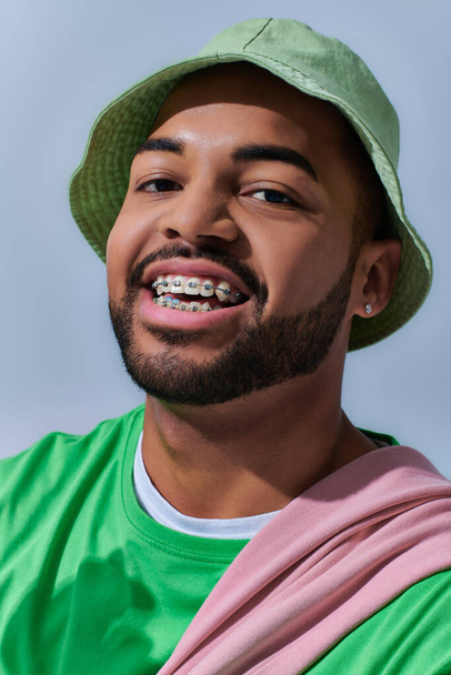 портрет веселого молодого человека в стильной Панаме с брекетами счастливо улыбаясь, концепция моды - Фото, изображение