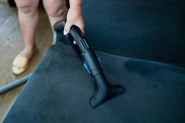 Cleaning service company employee removing dirt from furniture in flat with professional equipment. Female housekeeper arm cleaning sofa with washing vacuum cleaner close up. High quality photo - Фото, зображення