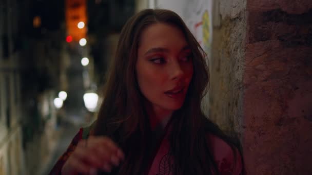 Gorgeous model standing urban street late evening looking camera confidently close up. Portrait of attractive glamorous woman leaning at city building wall in front night city lights. Town nightlife. - Footage, Video