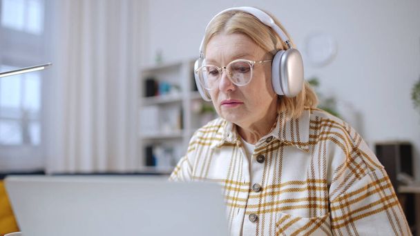Woman in her 50s taking online lesson in headphones, video course, senior student - Foto, afbeelding