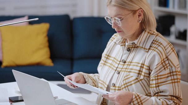 A woman in her 50s is working on her laptop from home, a financial analyst, freelancer - Zdjęcie, obraz