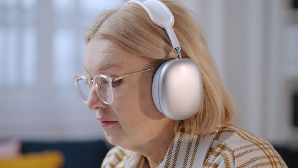 A serious senior woman in headphones is starting her workday in her home office as a freelancer - Fotografie, Obrázek