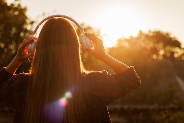 Junge Frau mit Kopfhörern hört Musik bei Sonnenuntergang. - Foto, Bild