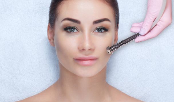 Le cosmétologue effectue la procédure Microdermabrasion de la peau faciale d'une belle jeune femme dans un salon de beauté.. - Photo, image