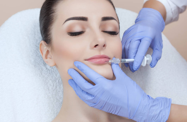 El médico cosmetólogo hace el procedimiento de aumento de labios de una mujer hermosa en un salón de belleza.. - Foto, Imagen