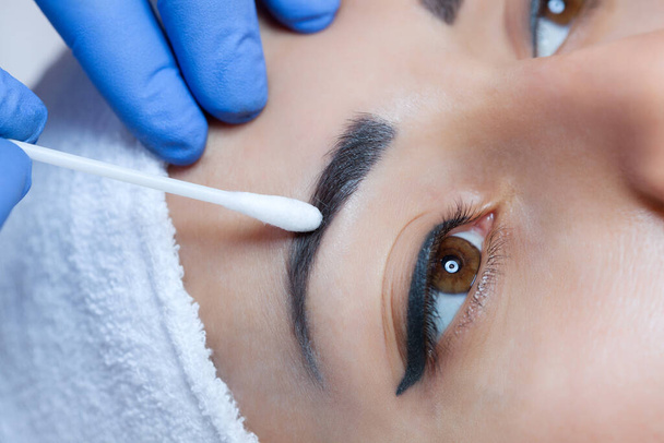 Permanent make-up for eyebrows of beautiful woman with thick brows in beauty salon. Closeup beautician doing  tattooing eyebrow. - Photo, Image