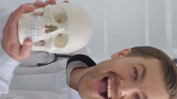 Молодий лікар тримає в кабінеті модель анатомічного черепа людини. Невролог розважається під час роботи. Вертикальне відео - Кадри, відео