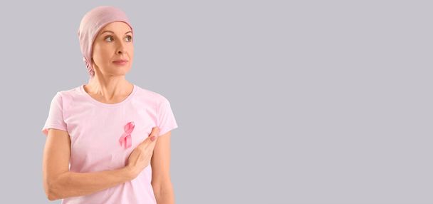 Mujer madura después de la quimioterapia con cinta rosa sobre fondo gris con espacio para texto. Concientización sobre el cáncer de mama - Foto, Imagen