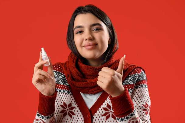 Sairas nuori nainen, jolla nenätipat osoittavat peukalo ylös punaisella taustalla - Valokuva, kuva