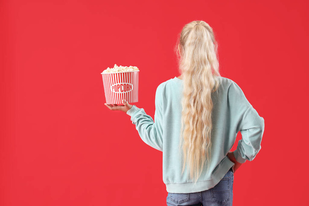 Dívka s kbelíkem popcornu na červeném pozadí, pohled zezadu - Fotografie, Obrázek