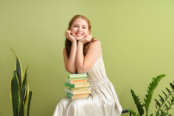 Yeşil duvarın yanında yığınla kitabı olan genç bir kadın. - Fotoğraf, Görsel