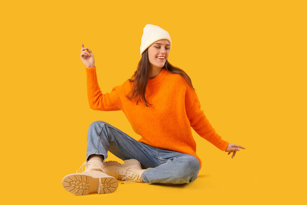 fiatal nő téli ruhák ül sárga háttér - Fotó, kép