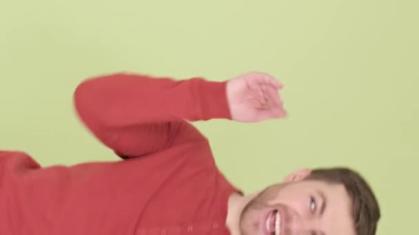 Ένας νεαρός με πορτοκαλί πουλόβερ χορεύει περίεργα απομονωμένος στο βάθος του στούντιο. Κάθετη βίντεο - Πλάνα, βίντεο