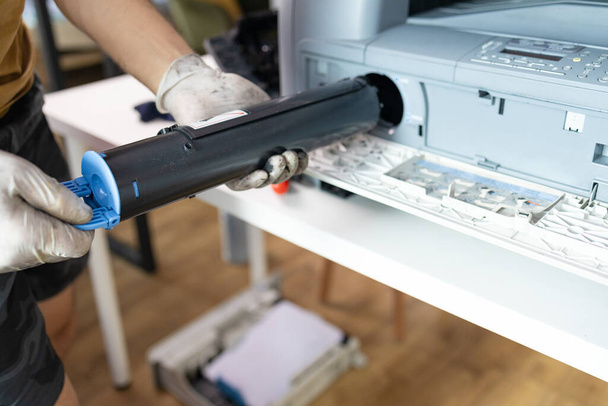 nyomtató javító technikus. Egy férfi ezermester megvizsgál egy nyomtatót, mielőtt elkezdené a javításokat a szervizközpontban.. - Fotó, kép