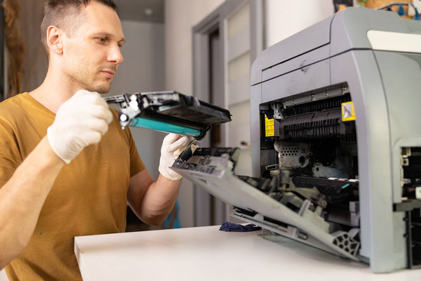 printerreparateur. Een mannelijke klusjesman inspecteert een printer voordat hij met reparaties in het servicecentrum begint.. - Foto, afbeelding