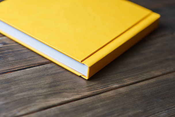 Yellow hardcover photobook isolated on a wooden background with copy space. Perspective view. Blank closed book mockup for placing custom text or images. Promoting printing photos from photoshoot. - Photo, Image