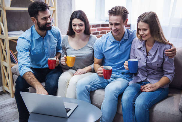 Les jeunes gens d'affaires utilisent un ordinateur portable, boivent du thé, parlent et sourient tout en passant du temps ensemble à la maison
 - Photo, image