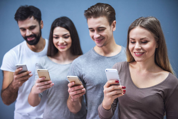 Hermosos jóvenes están utilizando teléfonos inteligentes y sonriendo, sobre un fondo gris
 - Foto, imagen