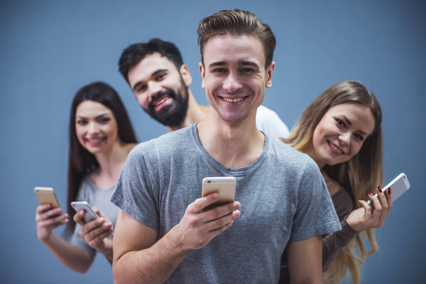 Güzel genç insanlar akıllı telefonlar kullanarak ve gri arka plan üzerinde gülümseyen - Fotoğraf, Görsel