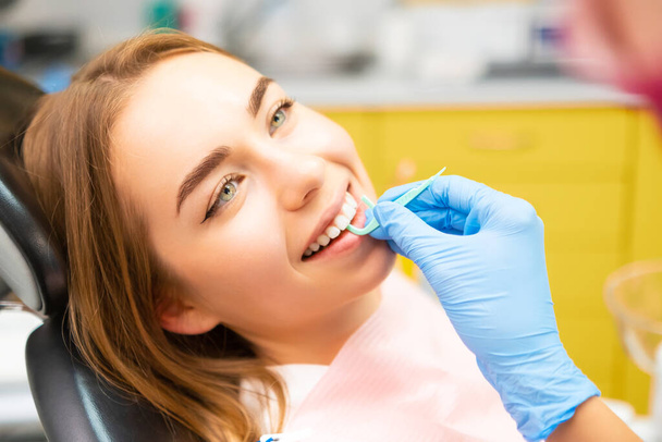 Дантист рассказывает молодой женщине об использовании зубной нити во время посещения стоматологической практики. - Фото, изображение