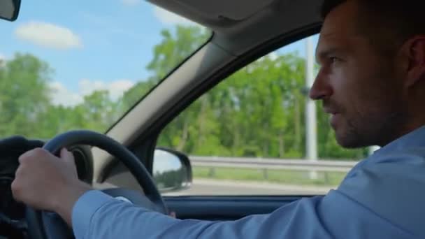 Ευτυχισμένος νεαρός άνδρας κρατώντας το χέρι στο τιμόνι στα δεξιά με θέα στην πόλη. Πλευρική άποψη. Δεξί τιμόνι. Τρόπος ζωής, ταξιδιωτική έννοια. Πραγματικός χρόνος - Πλάνα, βίντεο