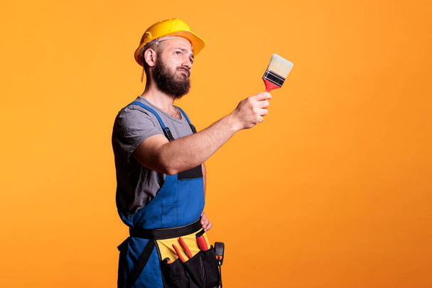 Muž dodavatel drží štětec k barevným stěnám, pracuje na projektu rekonstrukce a malování s nástroji. Stavební dělník dělá renovační práce se štětcem a nátěrem. - Fotografie, Obrázek