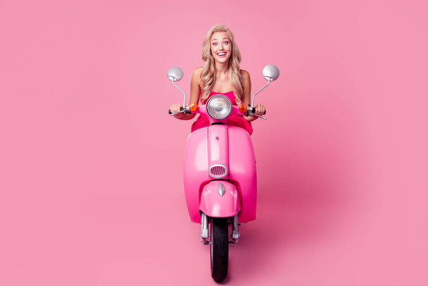 Full length photo of pretty excited girl dressed sexy outfit driving moped hurrying party isolated pink color background. - Zdjęcie, obraz