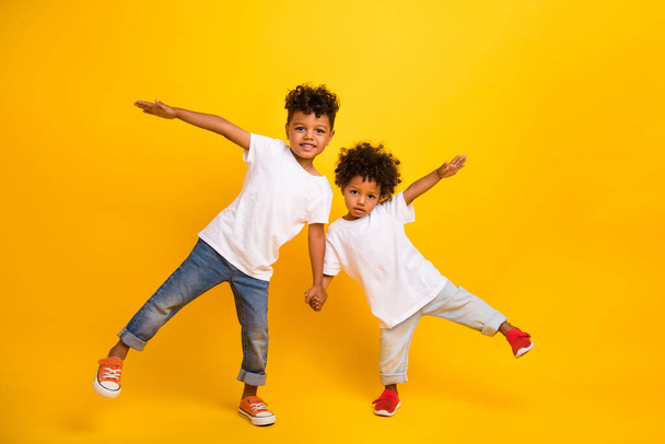 Full size photo of two small funky carefree people hold arms have fun dancing isolated on yellow color background. - Fotó, kép