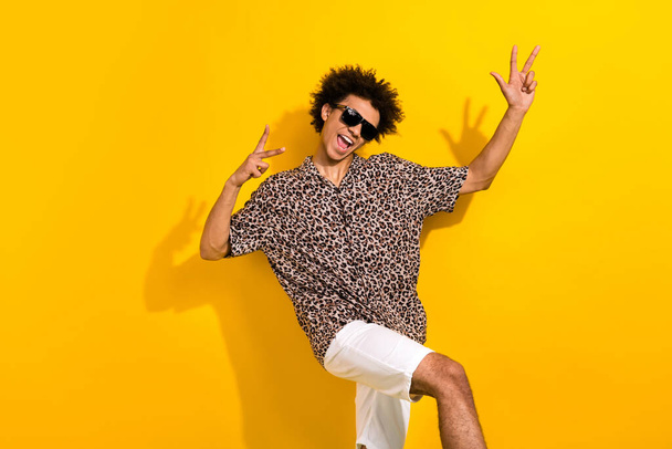 Photo of cheerful positive guy with afro hair dressed print shirt in sunglass dancing having fun isolated on yellow color background. - Foto, afbeelding