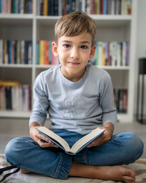 Кавказский мальчик учащийся ученик читать книгу дома на полу исследования узнать подготовиться к школе - Фото, изображение