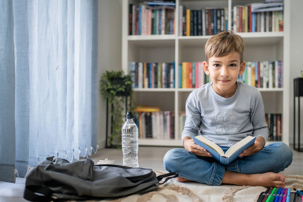 caucásico chico alumno estudiante leer libro en casa en el piso estudio aprender a prepararse para la escuela - Foto, imagen